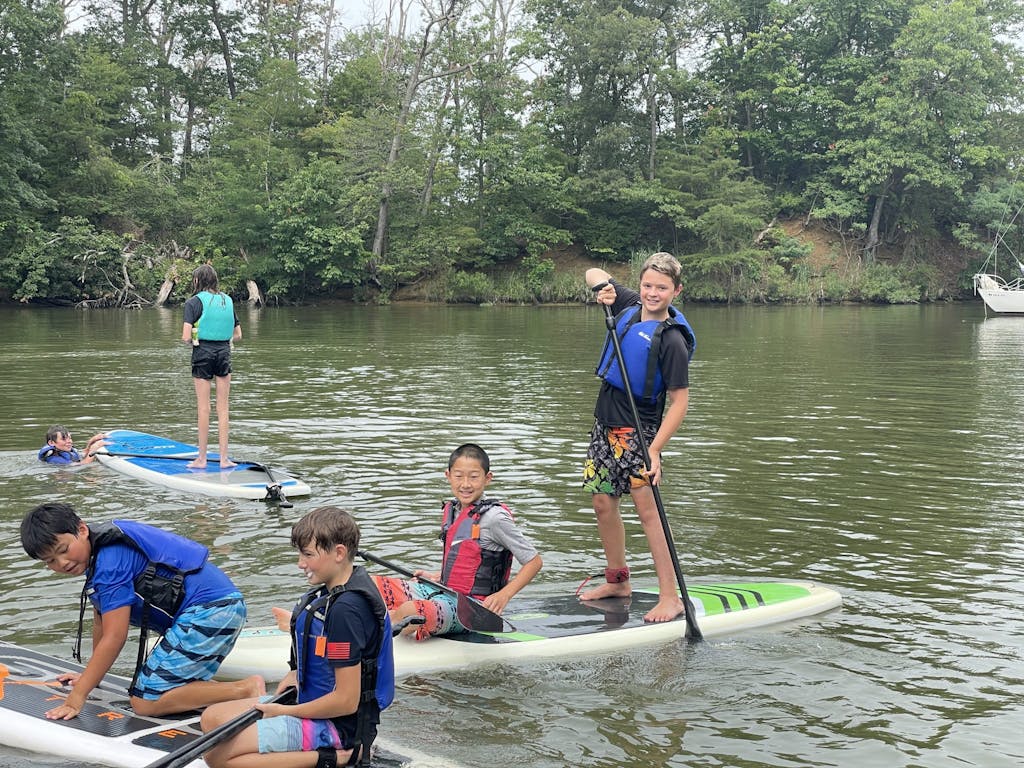 Grom campers standing and sitting on paddle boards on Back Creek
