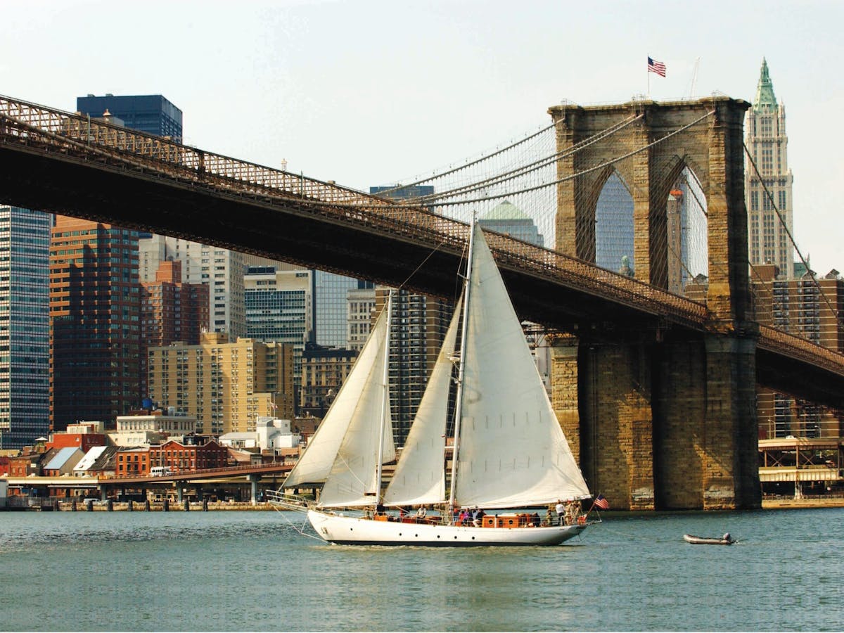 a large ship in a body of water with Brooklyn Bridge in the background