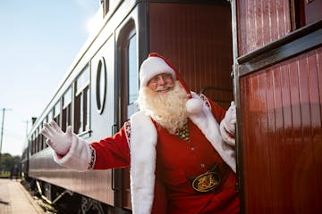 Santa leaning outside the train car while smiling and waving.