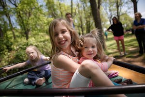 Three little girls playing outdoors on a merry go round while family members supervise at a family reunion.
