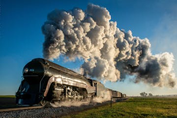 #611 train on a track at sunrise with smoke coming out of it.