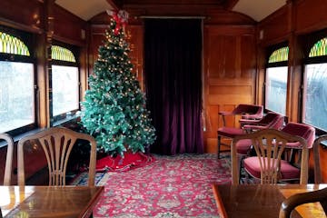 The club car on the train with tables, chairs, and a Christmas tree.
