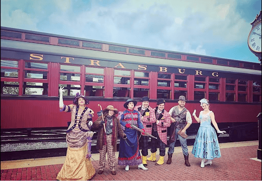 A group of seven historically-accurate Streetmosphere characters standing in front of a train at the Strasburg Rail Road.