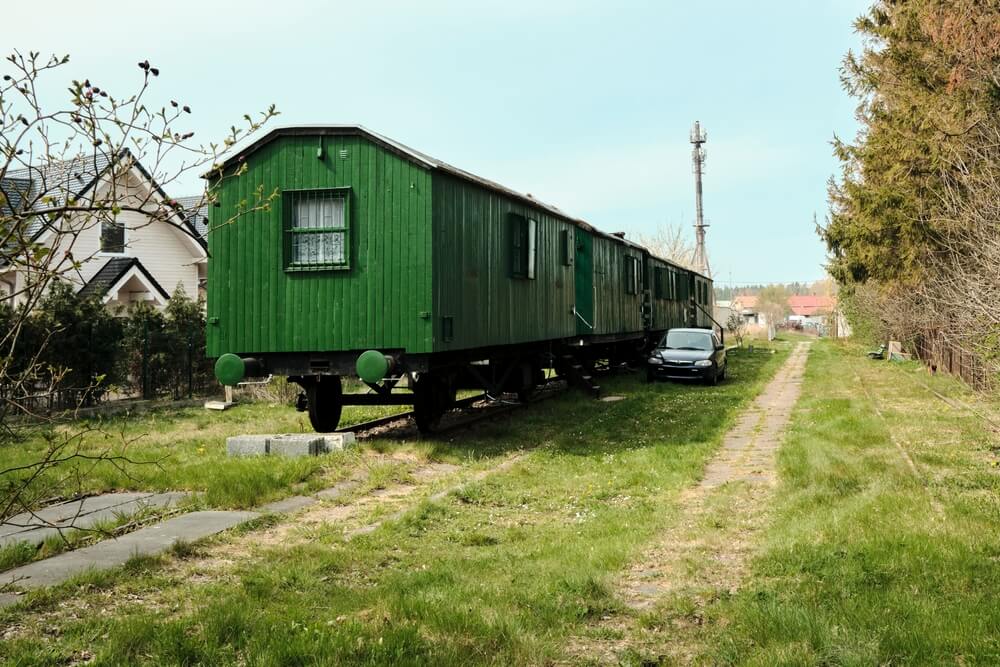 A train car home that is parked on an independent track among a lush green field.