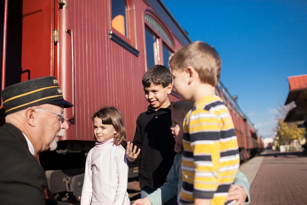 A train conductor talking to 4 children outside of a train.