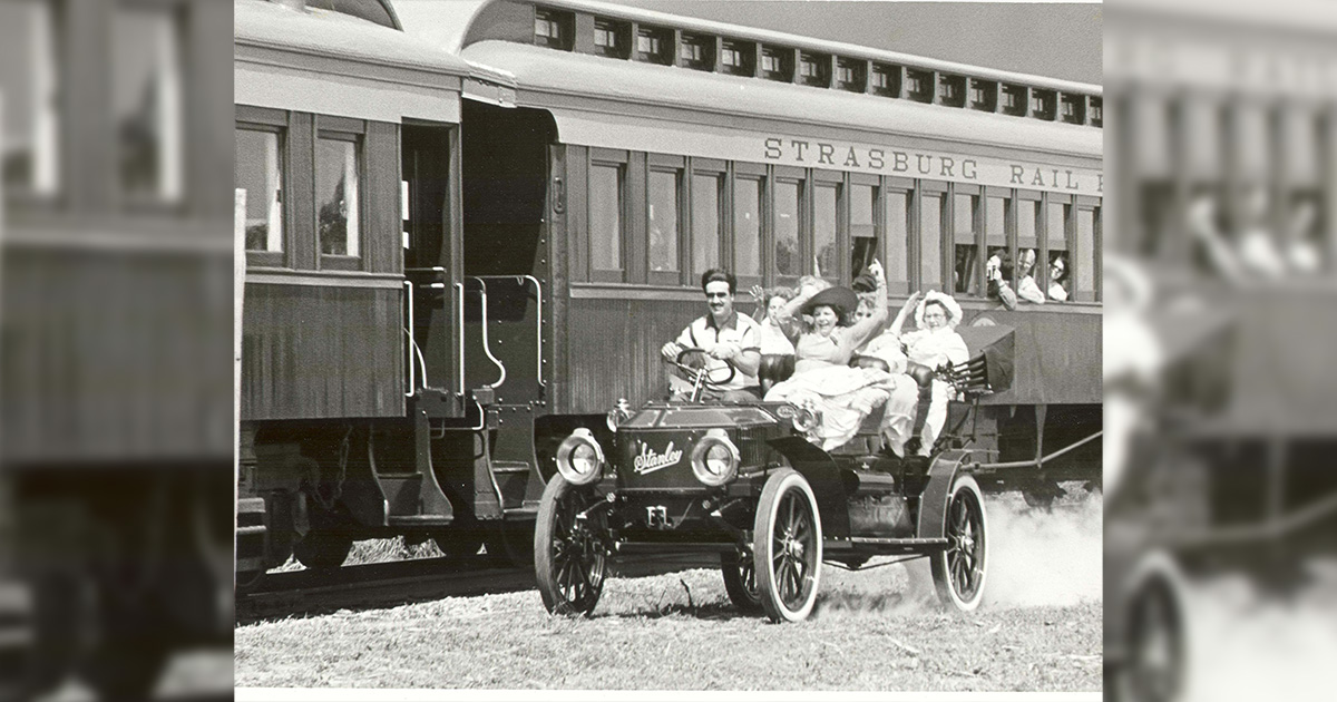 Old image of people riding in an automobile beside the Strasburg Rail Road.