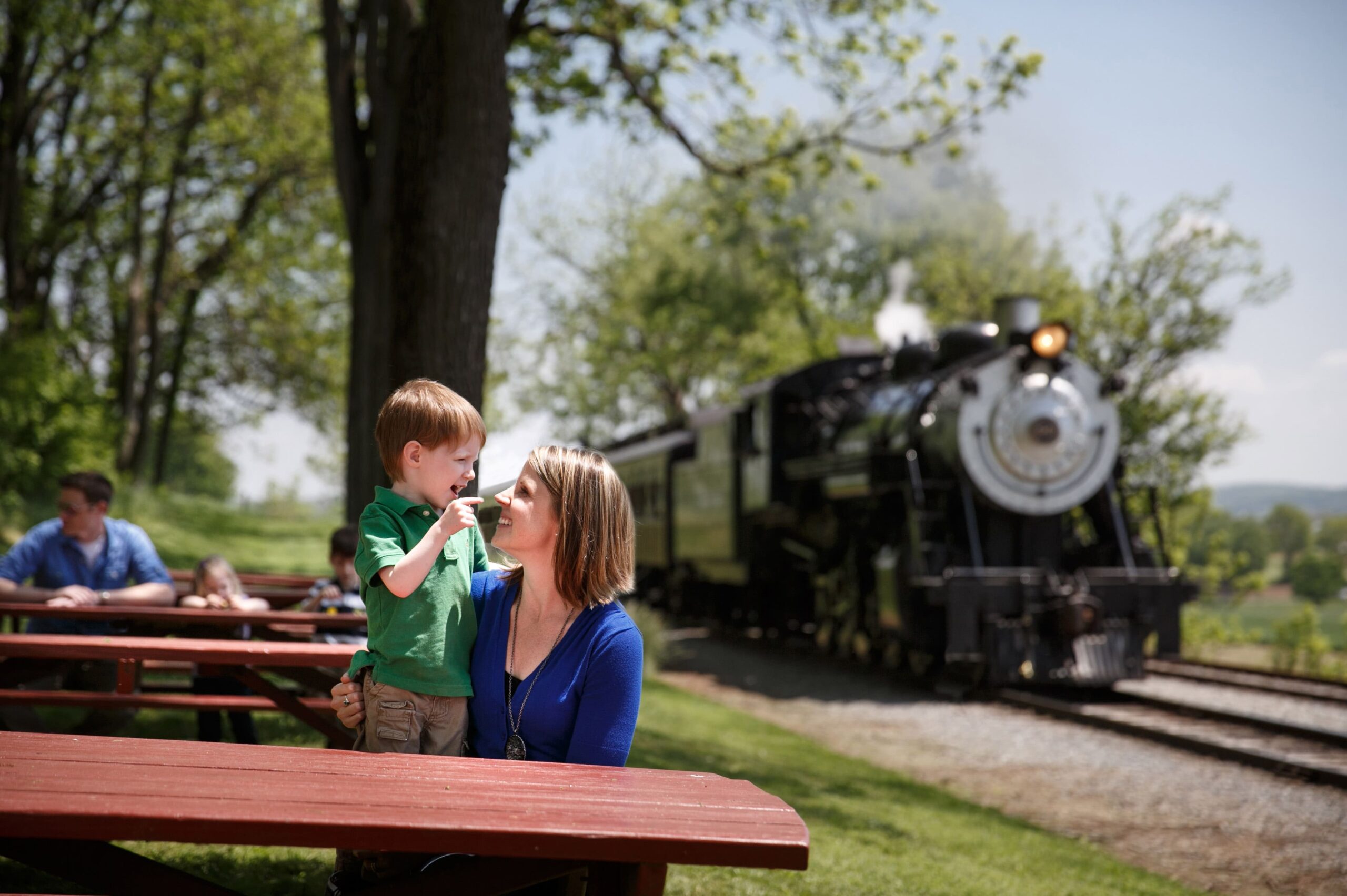 A close up on a mother and child in an outdoor picnic area with a train in the background.