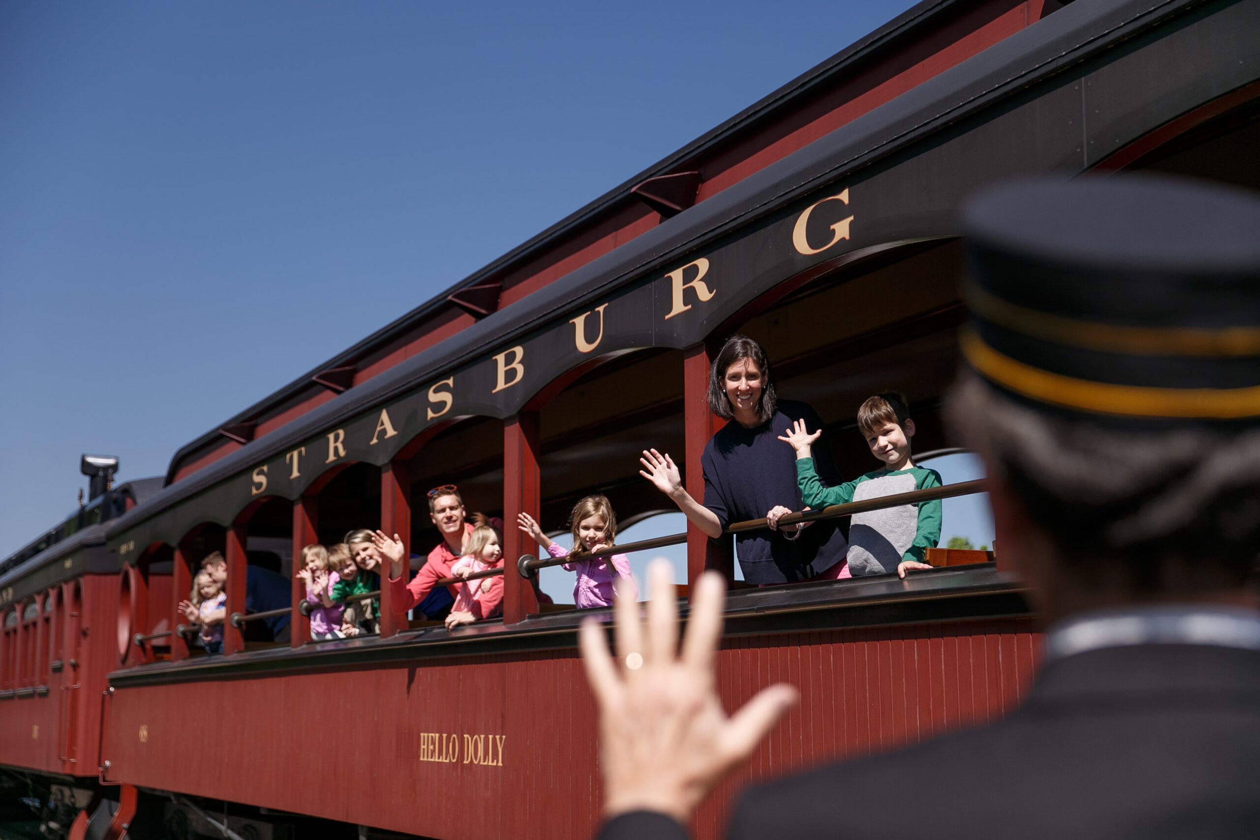 A railroad trainman waving to passengers aboard a train car waving back.