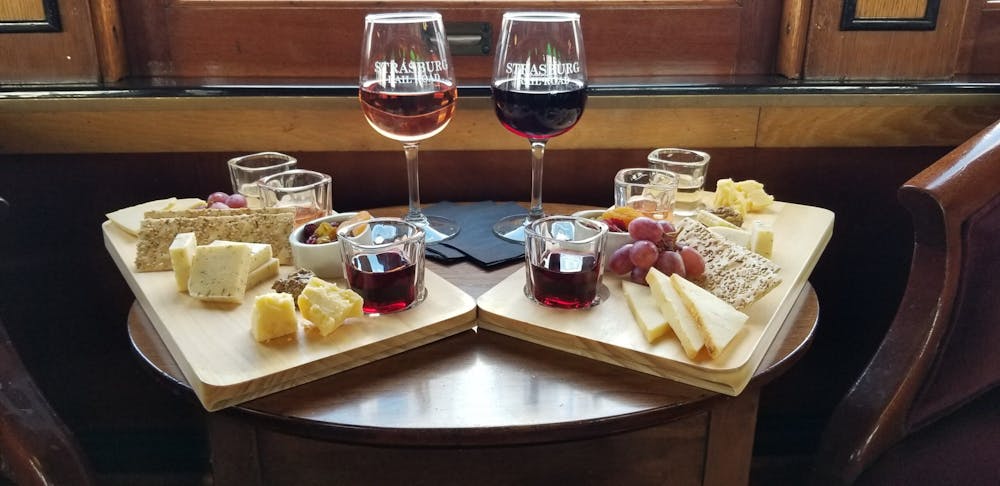 two glasses of wine and two cheese boards sitting on top of a wooden table