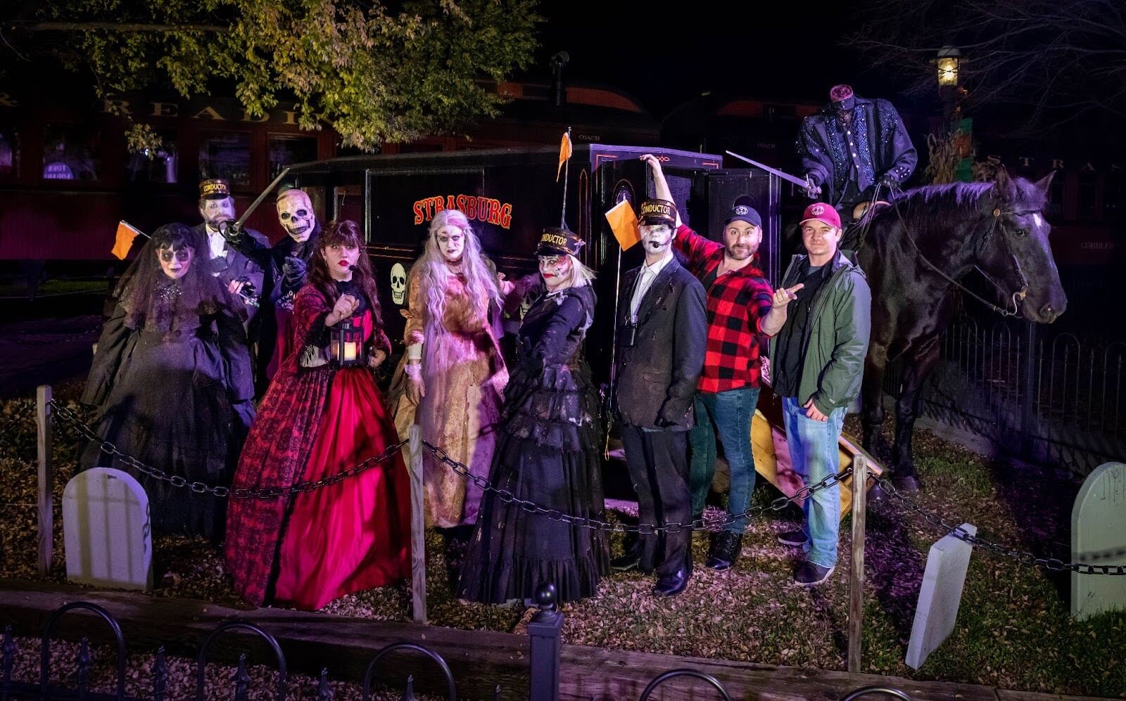 The cast of sleepy hollow dressed in spooky costumes posing for the camera next to a spooky horse and carriage.