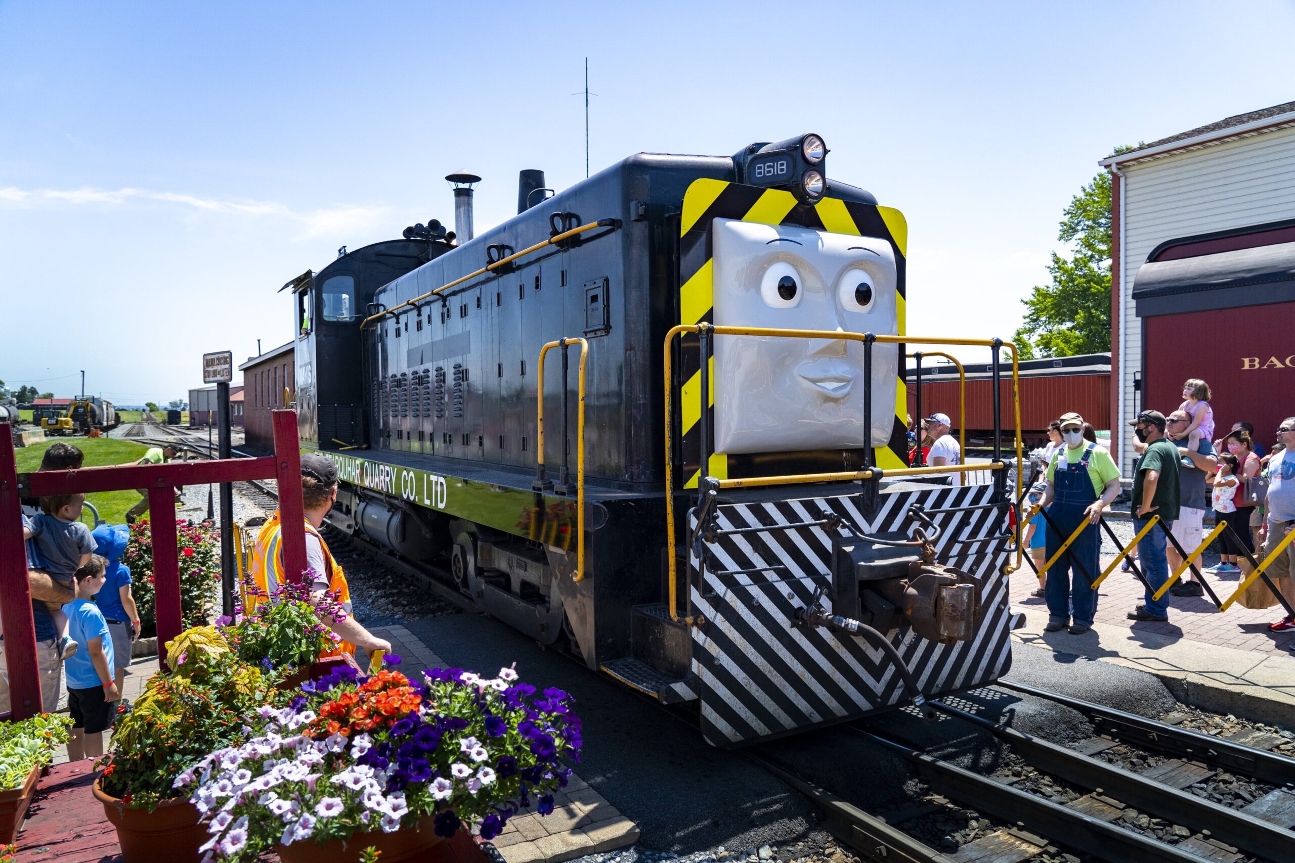 A group of people standing next to Mavis the train.