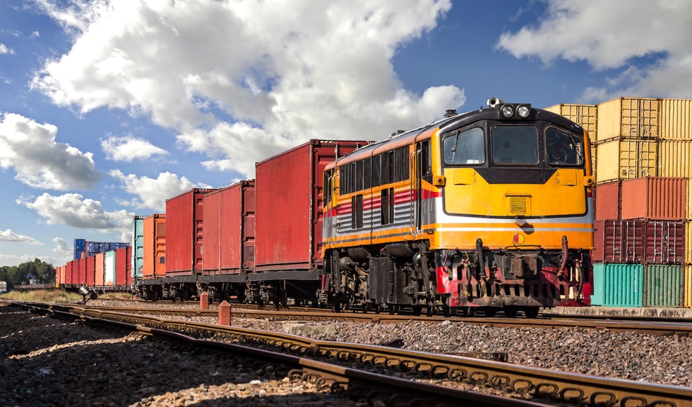 A container freight train outside with a cloudy sky.