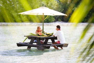 A couple having a lunch feet in the water on a motu in Bora Bora