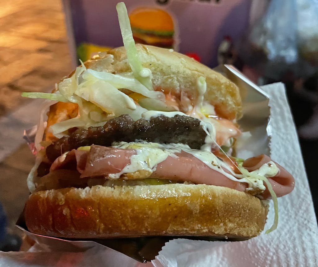 a close up of a hamburger in front of a street food cart