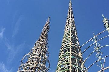 a large tall tower with a sky background with Watts Towers in the background