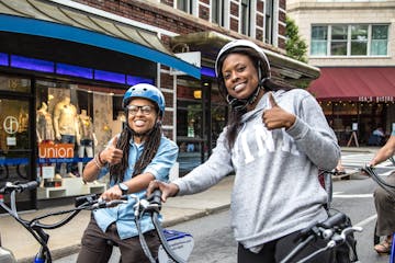 Two people are standing on e-bikes during a custom tour of downtown Asheville and smiling at the camera with two thumbs up!