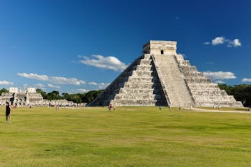 a large building with a grassy field with Chichen Itza in the background