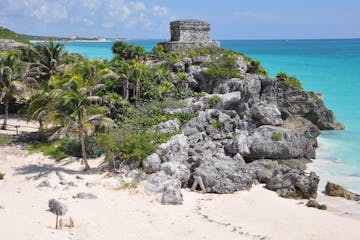 a rocky beach next to a body of water with Tulum in the background
