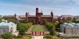 a large brick building with grass in front of a house with Smithsonian Institution in the background