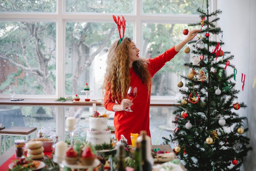 A woman in a red dress preparing a fun winter-themed party by decorating a Christmas tree