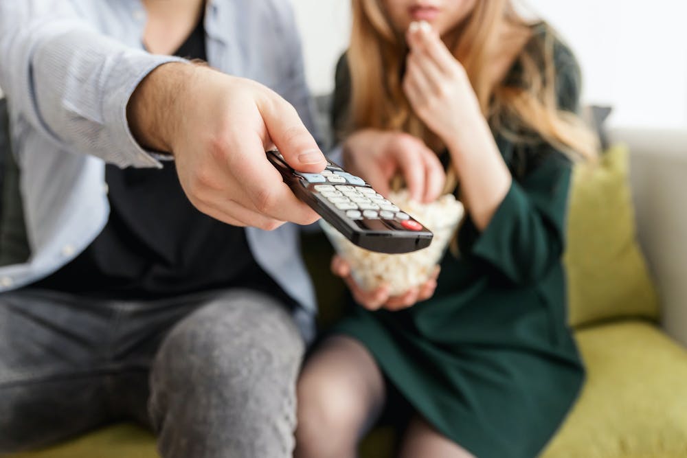 A man and woman sitting on a couch watching TV.