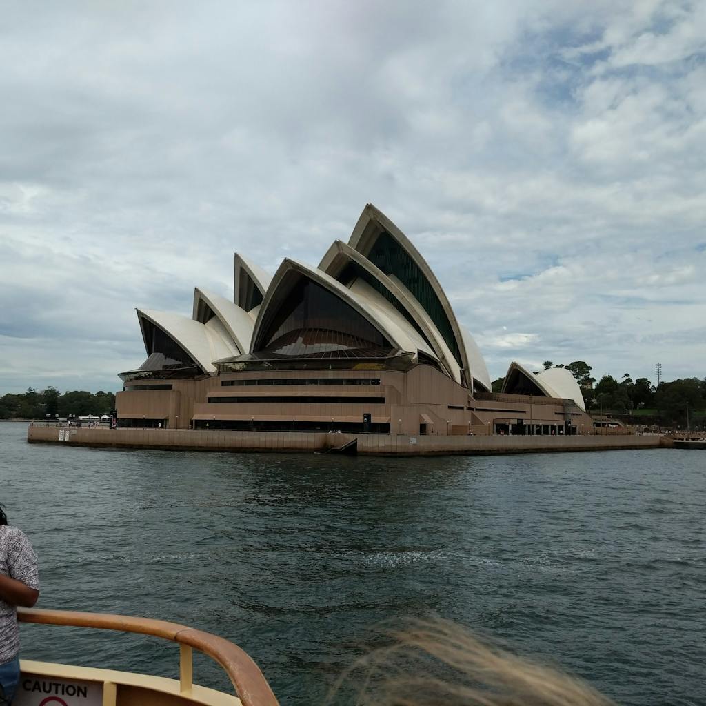 a wooden boat in a body of water with Sydney Opera House in the background