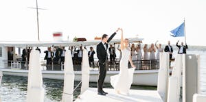 Bride and groom dancing on pier, while the Yacht Polaris cruises behind them with their bridal company cheering.