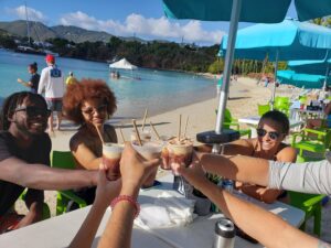 Guests 'cheersing' refreshing cocktails on at a table on the beach at Dinghy's Beach Bar, Water Island.