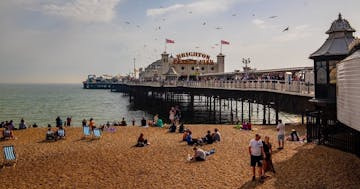 a group of people sitting at a beach with Brighton Pier Rock Shop in the background