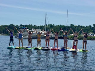 a group of young adults each on a stand up paddleboard on the water with their hands up excited