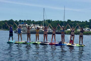 a group of young adults each on a stand up paddleboard on the water with their hands up excited