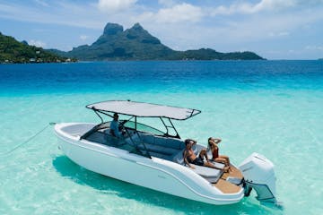 a blue and white boat sitting next to a body of water with Bora Bora in the background