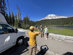 person taking a photo of people in front of trees and mountain