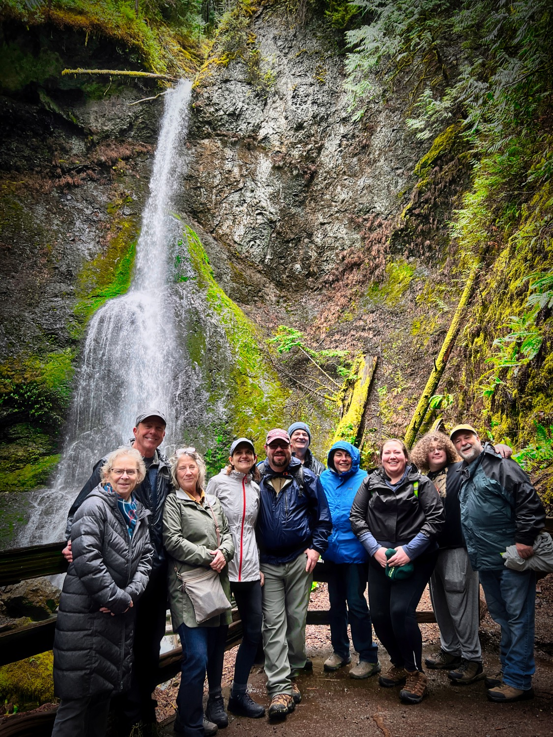 a group of people standing in front of Marymere Falls in the Olympic National Park