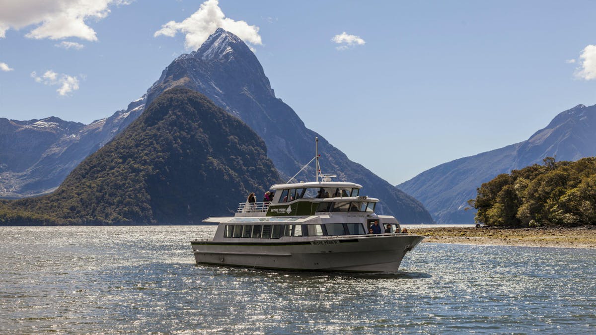 a small boat in a body of water with Milford Sound in the background