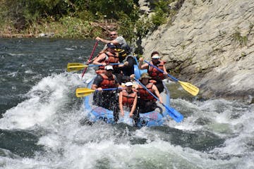 a group paddling a raft with a man in the back guiding over a rapid