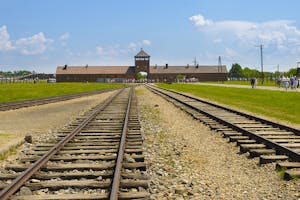 a large long train on a steel track with Auschwitz concentration camp in the background