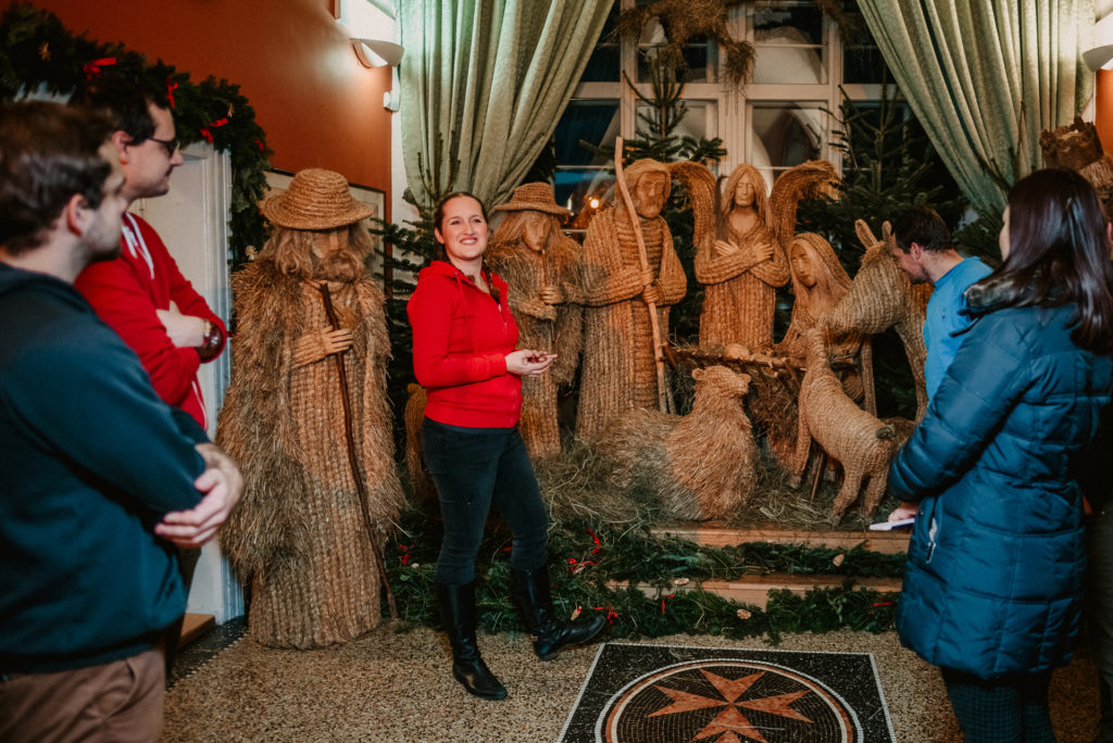 a tour guide showing a traditional Czech Nativity scene to a group of tourists on a Prague Christmas Markets tour