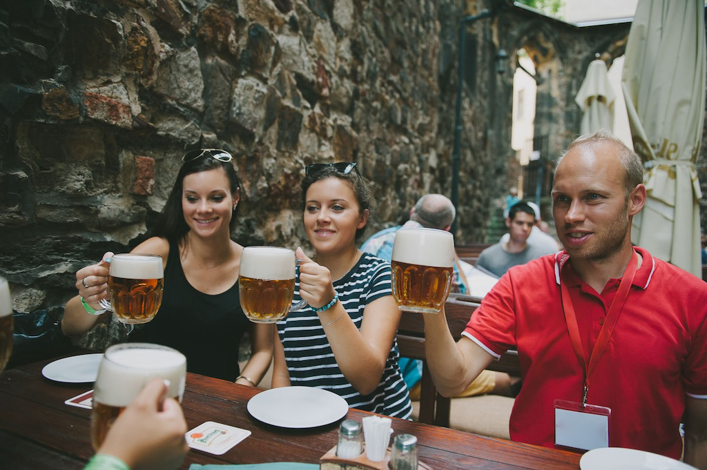 a group of people raising their beer glasses at the famous U Pinkasu bar in Prague's city center
