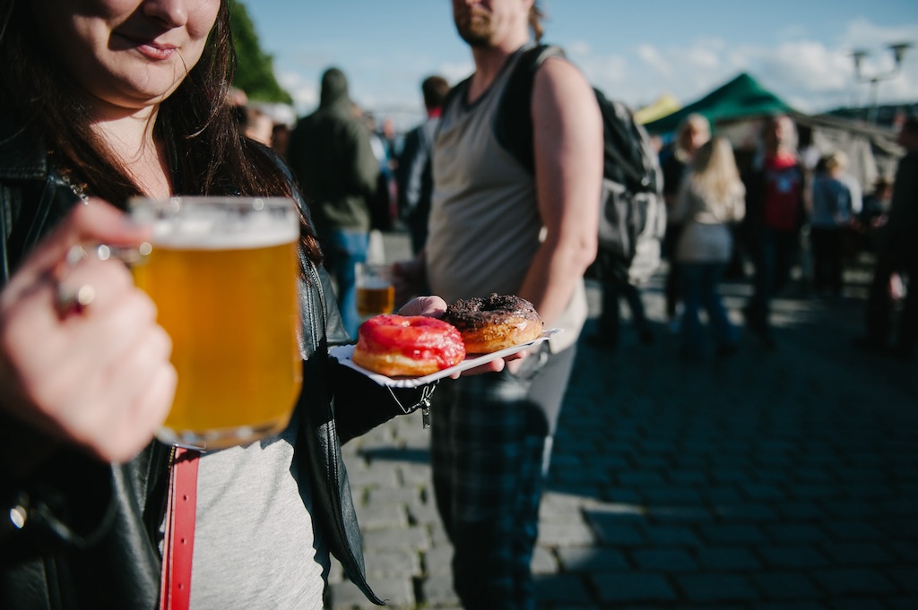a person holding a paper plate with donuts and a beer in the other hand during the Beer and Food festival in Prague