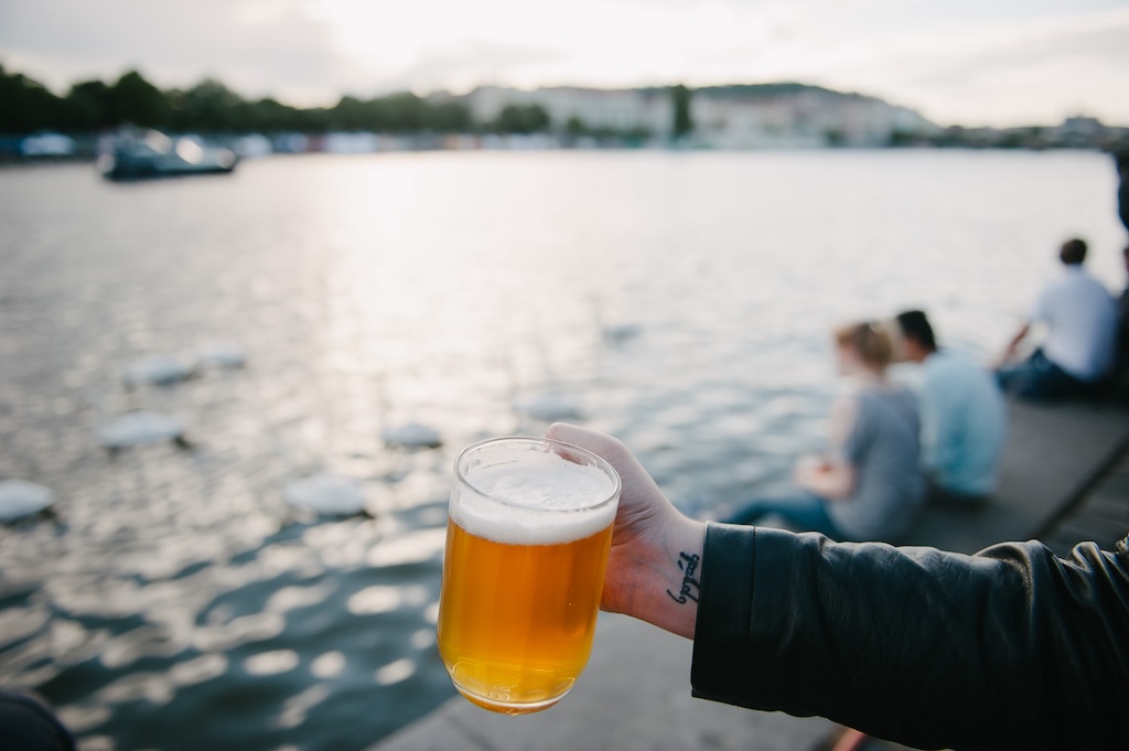 a person holding a glass of beer by the Vltava River in Prague