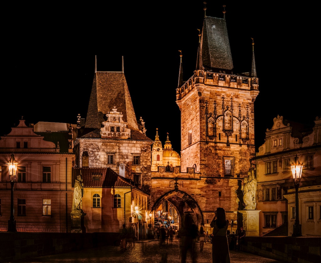 the medieval gate at the beginning of the Charles Bridge in Prague lit up by lights at night