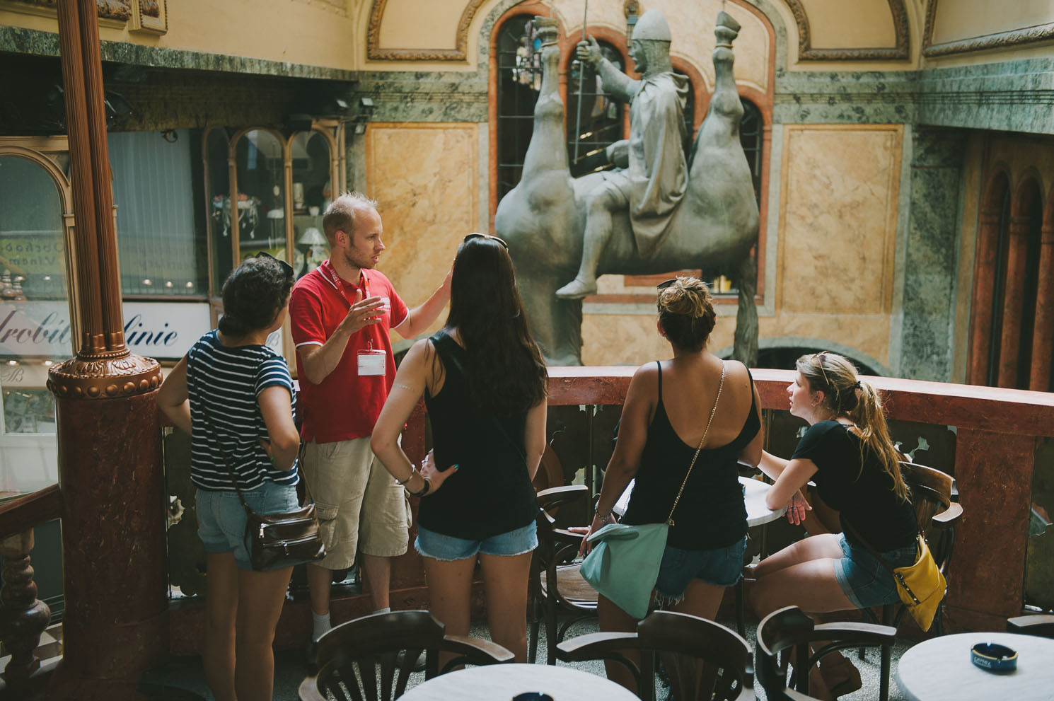 a group of tourists facing a tour guide explaining the statue of Wenceslas sitting on a horse upside down in one of Prague's most famous passages