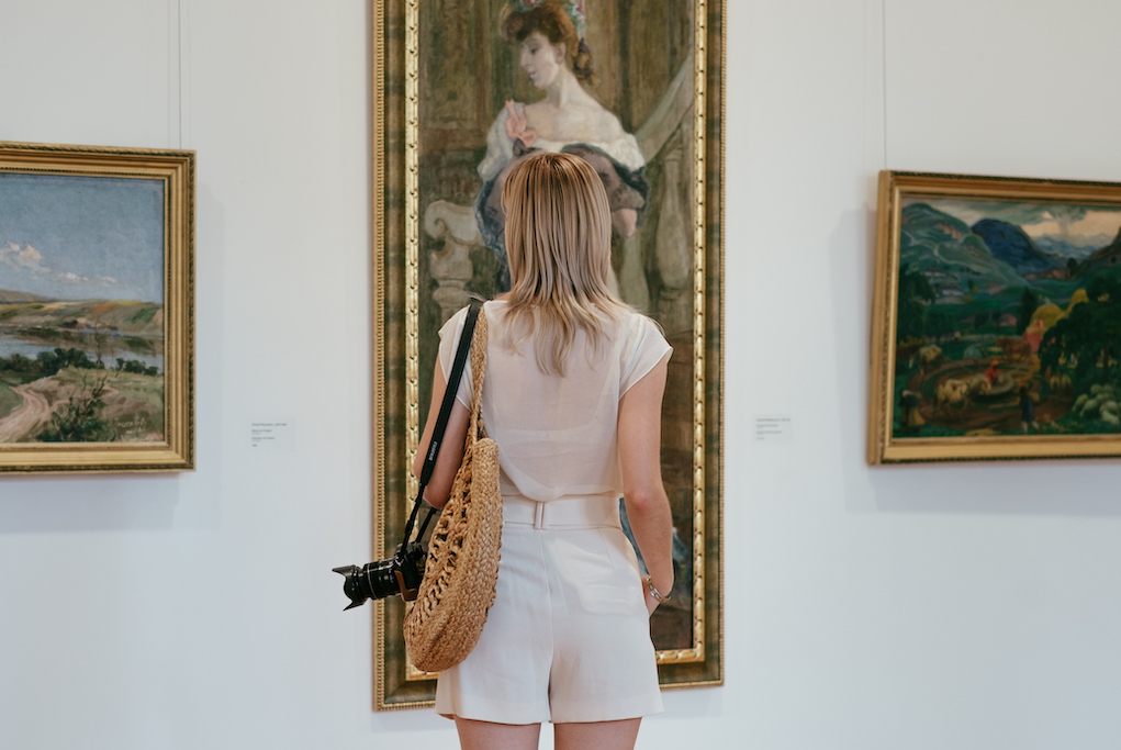 a woman standing in front of a painting hanging on a wall in an art gallery in Prague