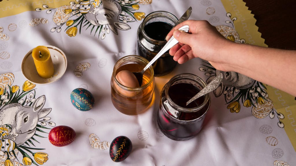 a hand putting an egg on a spoon into a mason jar with egg dye