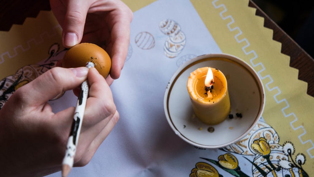 a candle and a hand decorating an egg