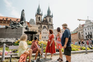 a group of tourists and a tour guide pointing at the Statue of Jan Hus in the Old Town Square of Prague