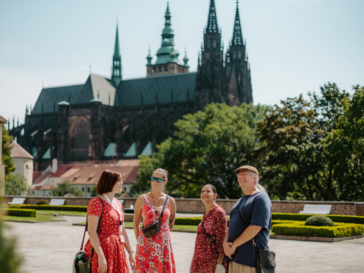 a group of tourists and a tour guide in one of the royal gardens of Prague Castle with a view of St. Vitus Cathedral in the background