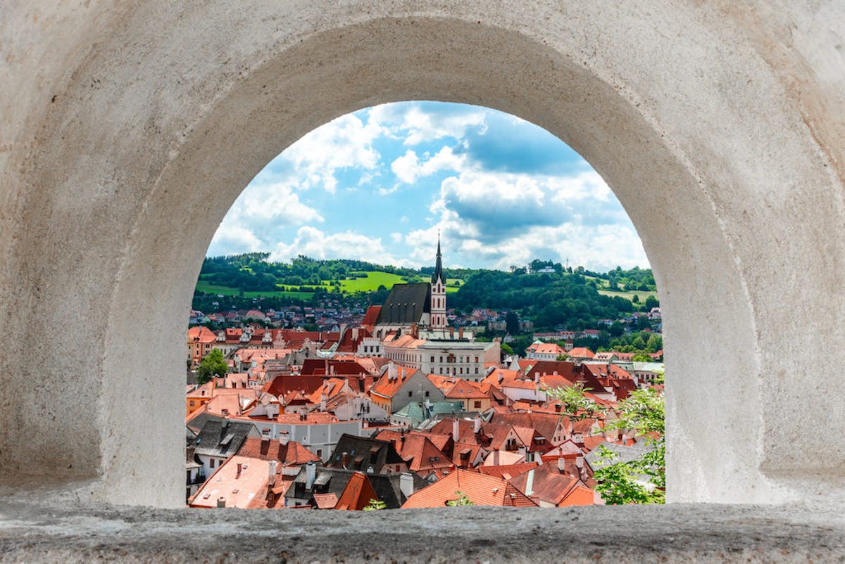 an arch-framed view of the historic city center of Cesky Krumlov with St Vitus church in the middle