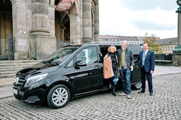 a couple of tourists standing beside their friendly looking driver and a comfortable looking van